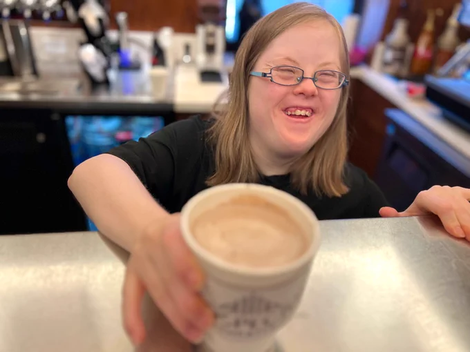 Margot smiles as she hands the camera a cup of coffee.