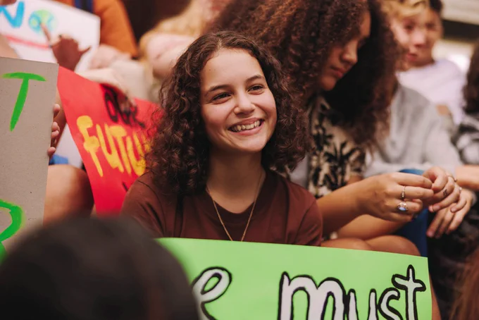 An image of a young woman holding a painted sign in a crowd of other people.