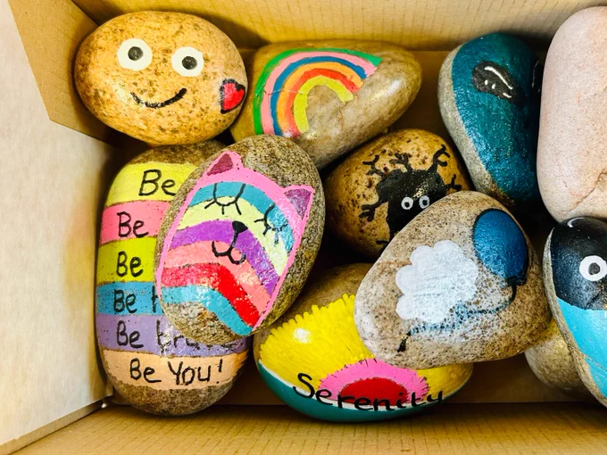 A selection of colourful rocks available to use in Churchill Library. A rainbow cat, a blue balloon, a smiley face and affirmation rocks.