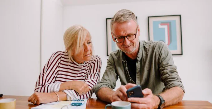 Image of a couple reading from and using a mobile phone together. 