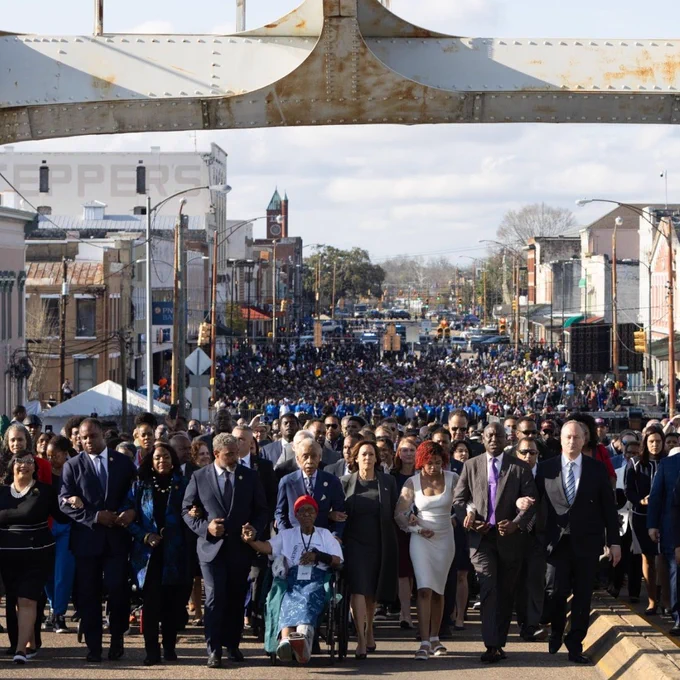 A large group of people marching across the Edmund Pettus Bridge in Selma, Alabama, with Vice President Kamala Harris marching front and center.