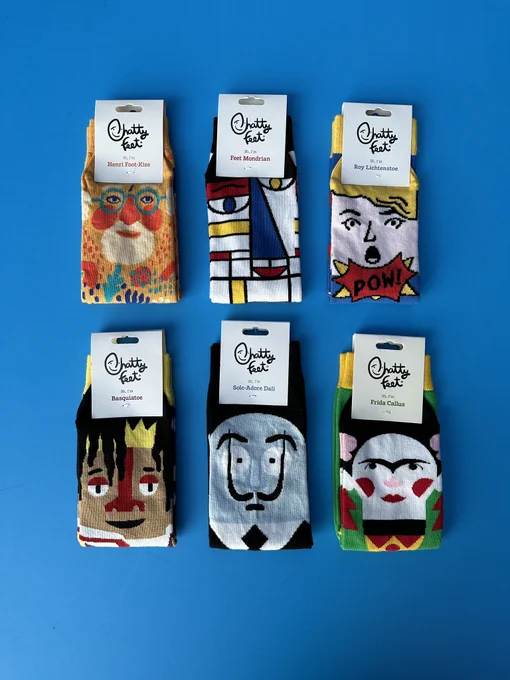 A photograph of 6 pairs of socks with different cartoon artist faces including Henri Matisse, Piet Mondrian, Roy Lichtenstein, Jean-Michel Basquiat, Salvador Dali and Frida Kahlo.