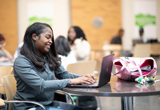 UNT student sitting with laptop at the G. Brint Ryan College of Business Leadership Building.