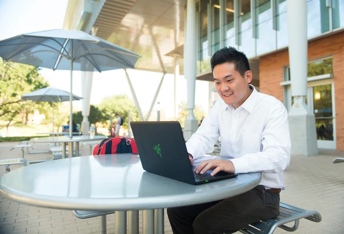 UNT student sitting with laptop outside of the G. Brint Ryan College of Business Leadership Building.