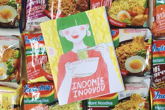 a zine titled "indomie indoyou" on a bed of packs of indomie instant noodles