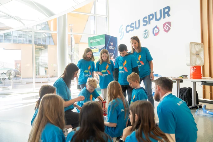 Group of kids and adults standing in a circle, some sitting on the ground