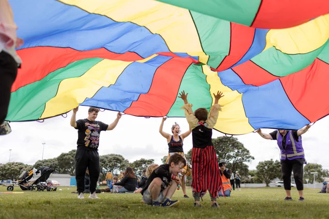 Adults and children playing together outside under a big colourful parachute. 