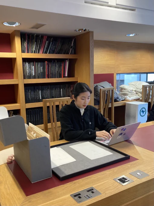Hyunjung An seated at a desk in the modern reading room. She is typing on a laptop and has Special Collections material out on the desk.