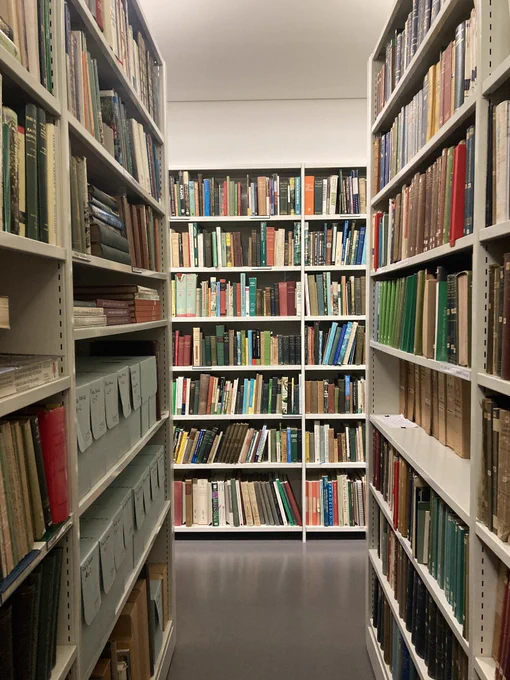 An aisle in a library with book shelves leading down to a corridor of more books.