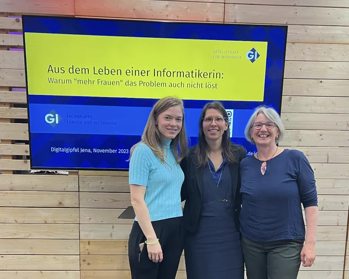 Drei Mitglieder der Fachgruppe vor einem Screen, auf dem eine PPT zu sehen ist: "Aus dem Leben einer Informatikerin – warum "mehr Frauen" das Problem auch nicht löst"