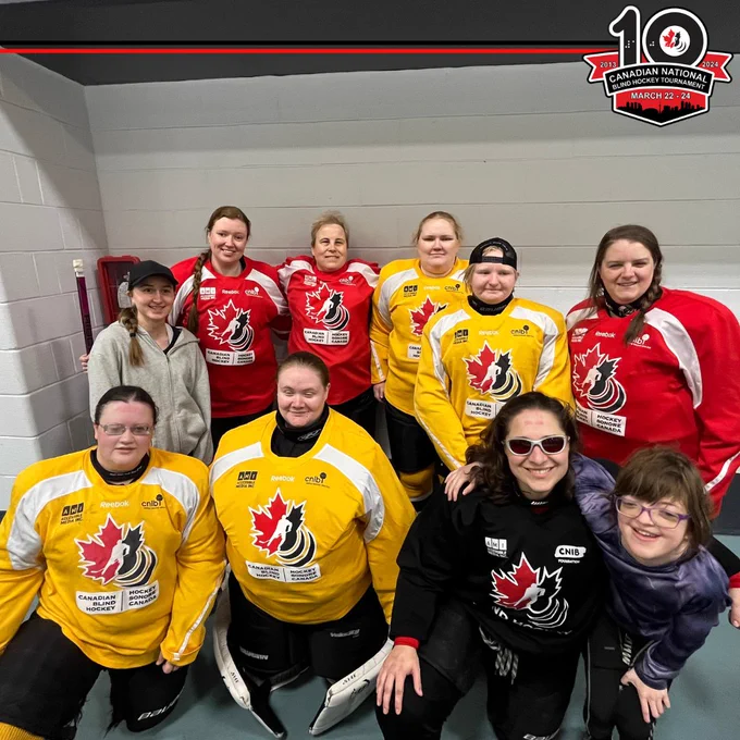 Amanda is pictured on the bottom right in this photo, wearing the black jersey. A group of 9 women smile for a photo during the summer development camp 2023