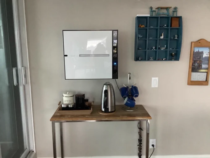 A modern living space featuring a Rabbit Air purifier on the wall next to a rustic table with coffee essentials and a decorative blue mug rack, enhancing the room's ambiance.