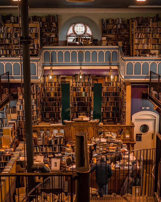 Image Description: Taken from a balcony looking down into a shop stacked with filled bookcases 
