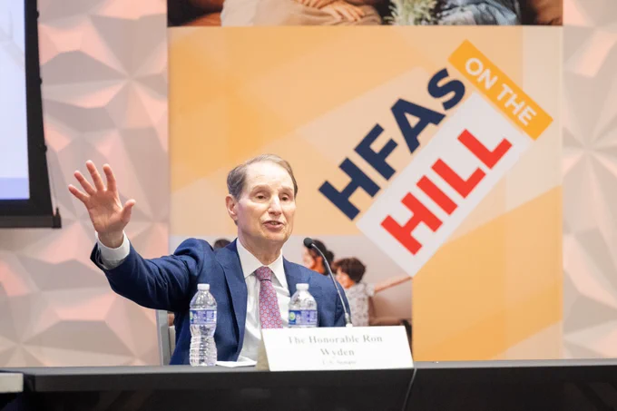 Senator Ron Wyden speaking at the NCSHA 2024 Legislative Conference with #HFAsOnTheHill sign in the background