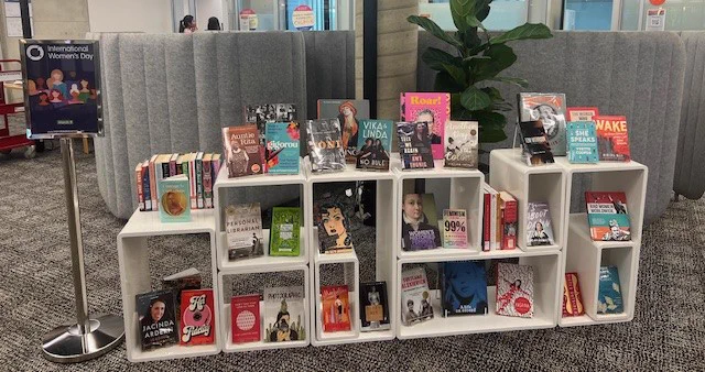 A large book display celebrating International Women's Day, with many books written by female authors. The books are displayed in white cube boxes and a sign is placed next to the display with the  International Women's Day 2024 theme. 