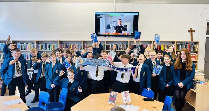 School pupils stood in front of a computer screen holding up their free World Book Day books