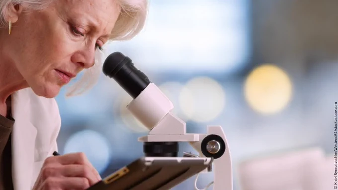 Female scientist looking into a microscope and making notes on a tablet.