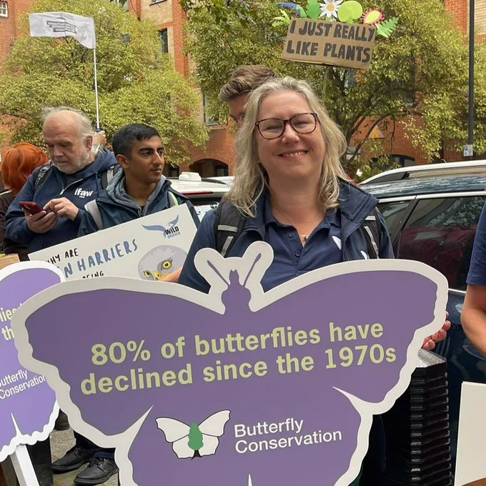 Head of Communications and PR Emma Butler holding a butterfly-shaped sign with the text '80% of butterflies have declined since the 1970s' and Butterfly Conservation logo