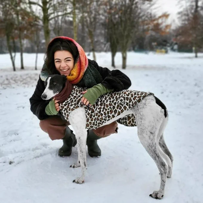 Youth Engagement Officer Emma Dakin crouched beside her greyhound in a snowy park