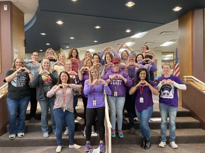 HMS staff members stand on stairs making hearts with hands