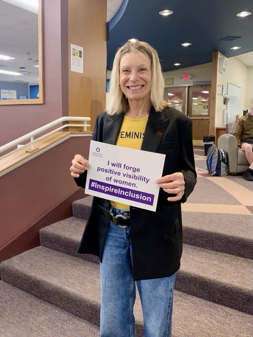 Teacher poses with sign "I will forge positive visibility of women." #Inspire Inclusion
