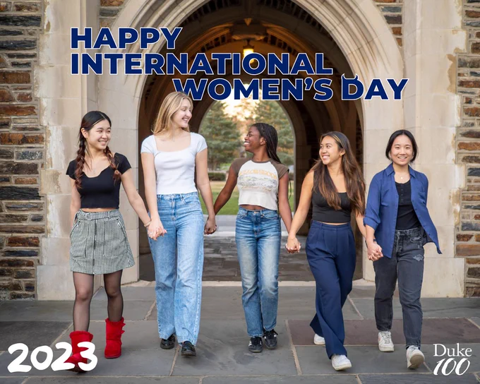 Five women walk under a stone archway at Duke holding hands. The year 2023 is written in the corner with the text "happy international women's day" at the top