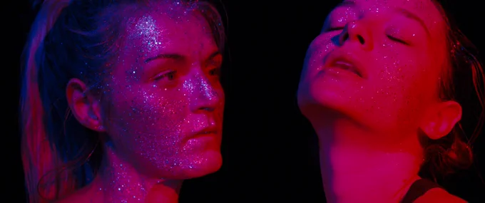 still from Silver Haze - two female faces covered in glitter, lit in neon pink
