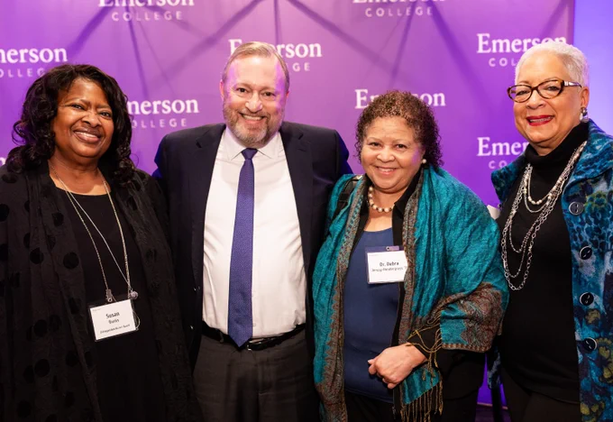 People pose and smile in front of a purple backdrop with the words "Emerson College."