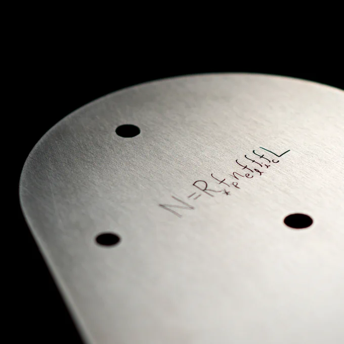 Detailed view of the Europa Clipper vault plate with the Drake Equation inscribed near the top. The vault plate is metal silver and the engravings are black, set against a black background. 