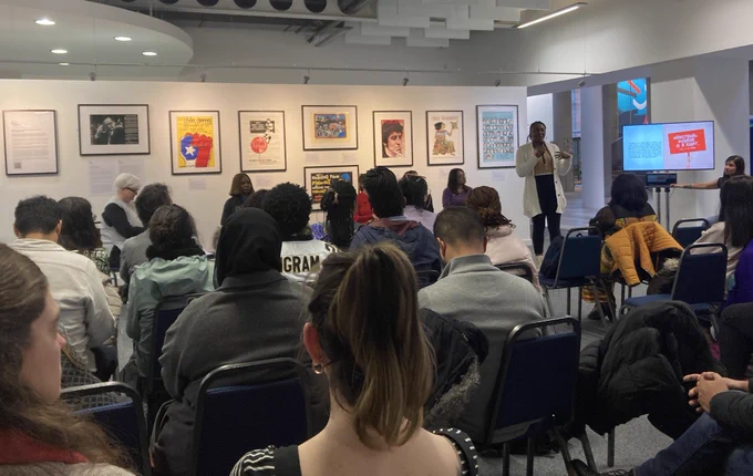 An audience watching a student deliver a presentation next to the exhibition wall of Chilean Solidarity Campaign posters in the GCU Archive Centre