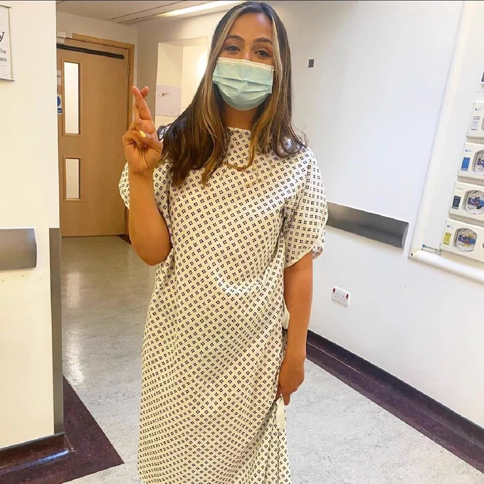 Hannah wearing a hospital gown and a face mask, while crossing her fingers.