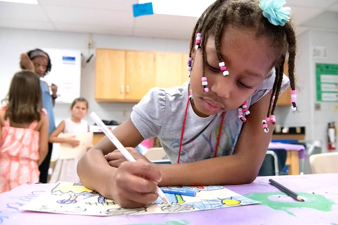 A student drawing on a piece of paper in a classroom.