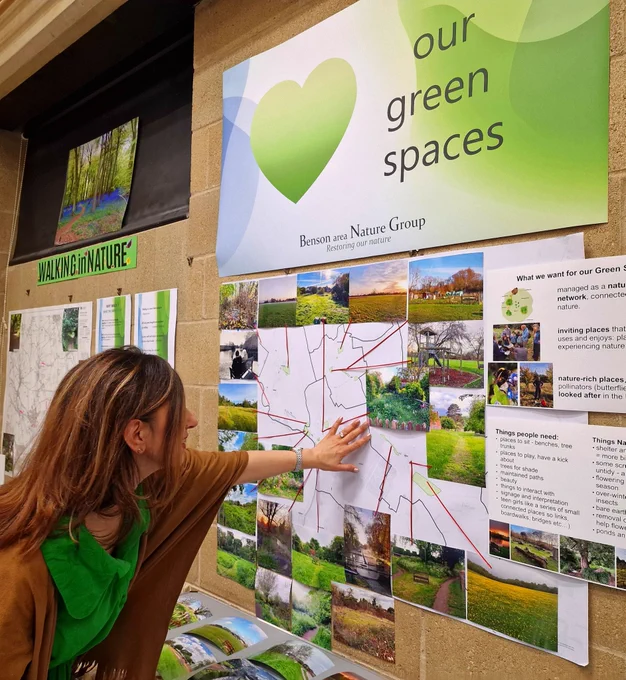 A woman (Geeta) at the Benson Nature event studying the 'Our Green Spaces' display with photographs and labels on Benson Nature features. Display created by Edel. 