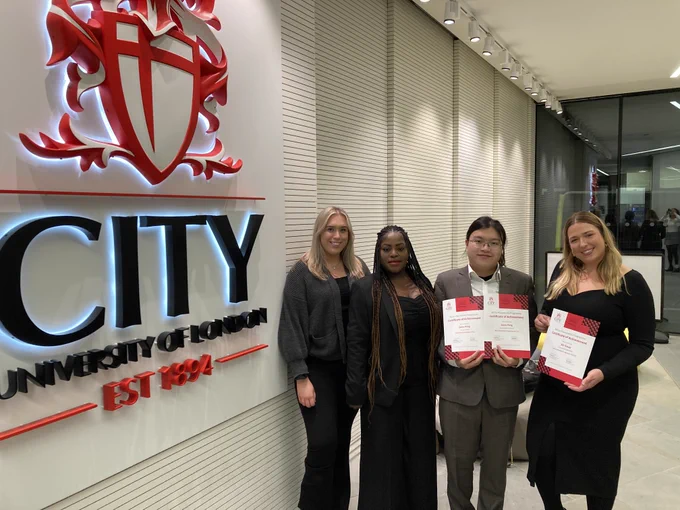 A group of students standing by the City logo holding up award certificates
