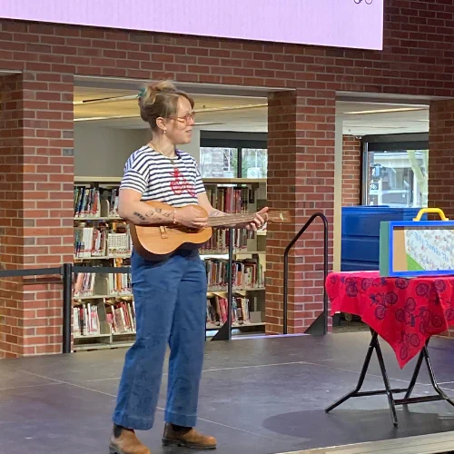 Lucy on stage at the Ann Arbor district library playing a ukelele