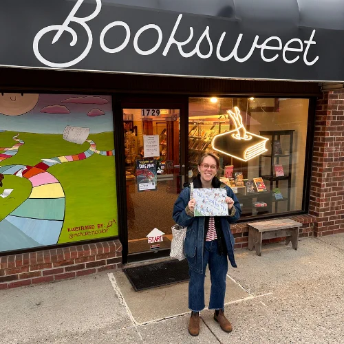 Lucy Knisley stands outside Booksweet holding a copy of Ride Beside Me
