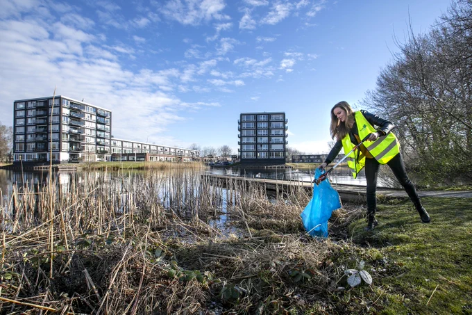 Foto van een vrouw die tijdens Landelijke Opschoondag afval prikt en het in een vuilniszak stopt