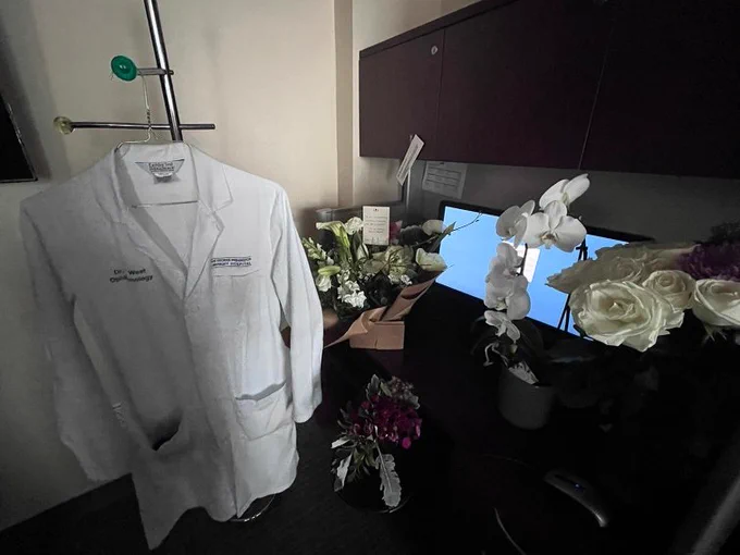 Dr. William West's desk in a resident workroom. Flowers adorn the desk and his white coat hangs to the side.