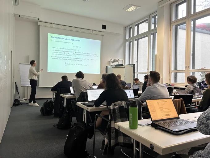 A snippet of 10 engaged participants in the seminar room with the lecturer Jannis Kück presenting.