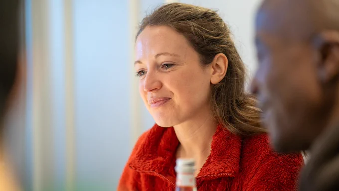 The image shows a woman in a red jacket looking down as if focusing on something, with a faint smile on her face.