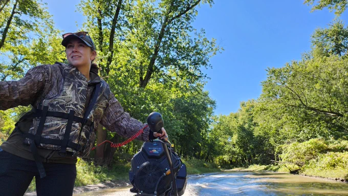 Madie McFarland driving a boat in a backwater slough along the Mississippi River while monitoring a DU conservation easement 