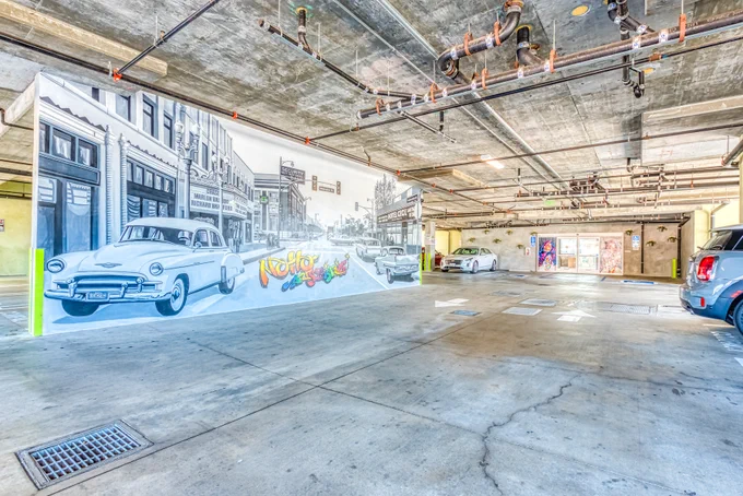 Lexen Hotel North Hollywood parking garage with wall mural of vintage car on Hollywood street and colorful text: NoHo Arts District.