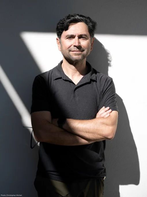 Ardem Patapoutian standing against a white wall. He is wearing a black t-shirt.