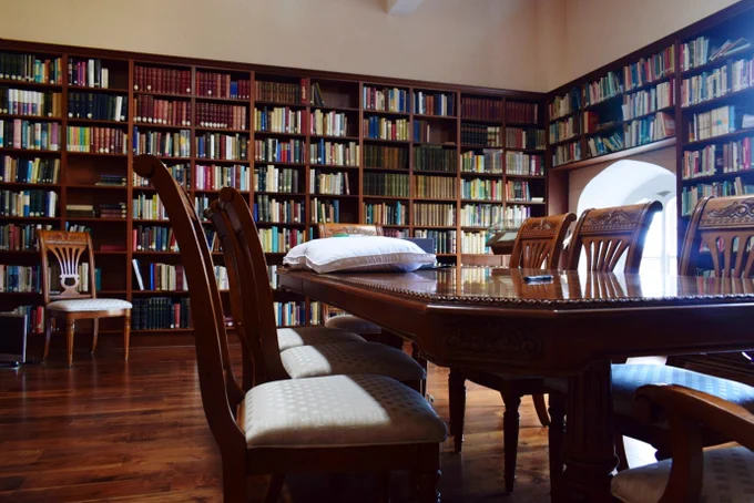 A reading room with walled book shelves. A chair sits in front of the shelves at the back of the room and a large table with chairs sits in the foreground of the picture. This is the Carrigan Reading Room, St. Kieran's College Kilkenny.