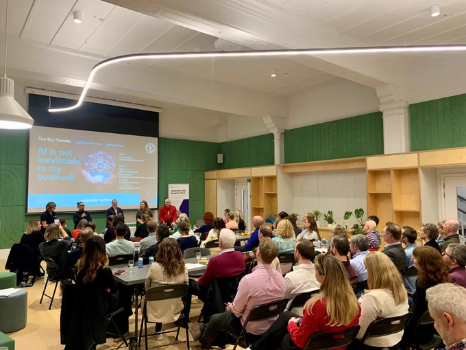 Seated attendees look towards a panel at the front of an event space 