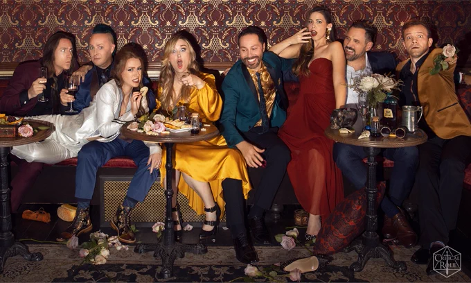 Matthew Mercer, Taliesin Jaffe, Ashley Johnson, Marisha Ray, Sam Riegel, Laura Bailey, Travis Willingham and Liam O'Brien pose together in a mashed together group shot dressed in their fanciest against the backdrop of a gorgeous hotel barroom interior in this photo 