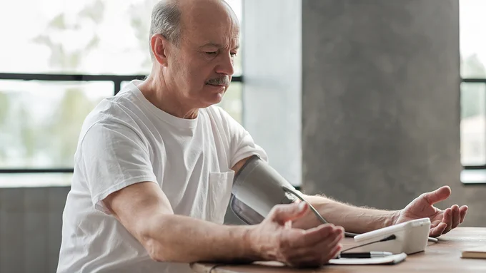 A middle aged adult taking their blood pressure with a self-measuring blood pressure machine.