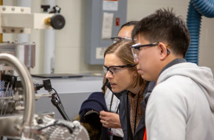 A woman in safety spectacles is looking at a thin-film of diamond growing.