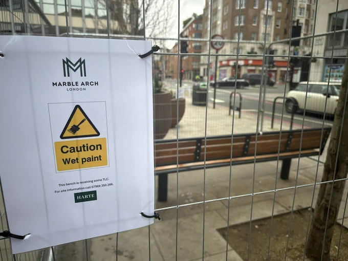 Bench at Burwood Place viewed through Heras fencing. Wet paint sign.