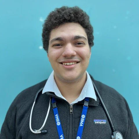 Portrait of Dr Fayez from Imperial College Healthcare. He has black, curly hair and is wearing a blue shirt, grey jumper and a stethoscope around his neck.